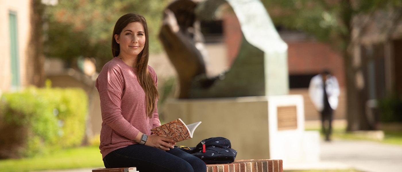 English student reading a book outside on campus courtyard