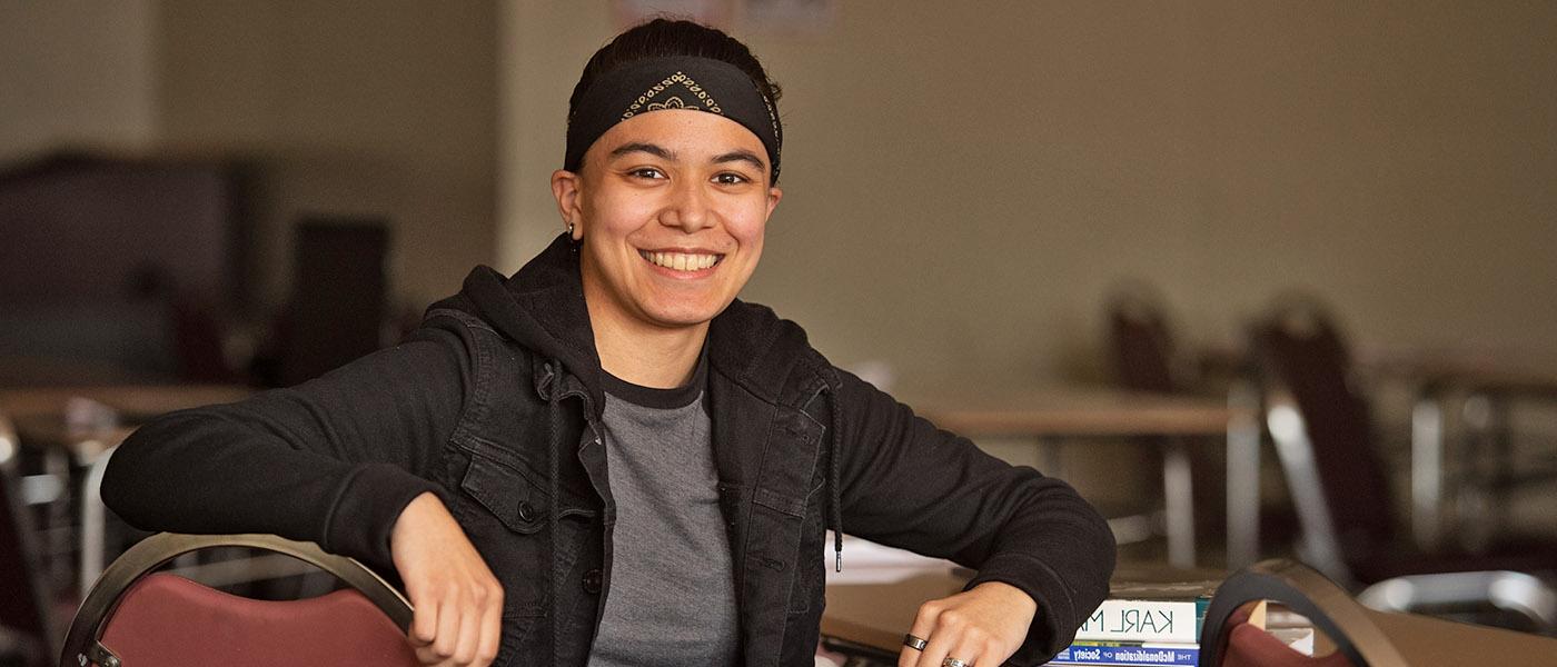 Smiling sociology student sitting in a desk with a few books on it